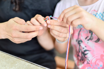 Hands of an adult and hands of a child knitting together