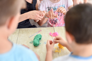 Hands of an adult and hands of a child knitting together