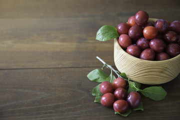 Garden plum in a wooden bowl on wooden background