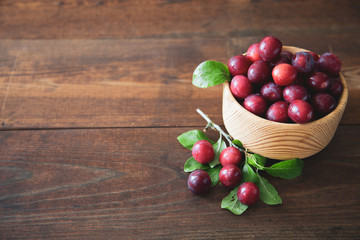 Garden plum in a wooden bowl on wooden background