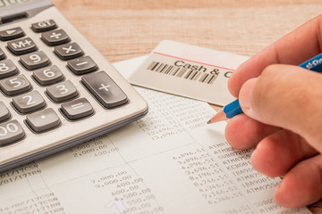 Fototapeta premium The fingers are holding the pencil. Below is a calculator, a bank book, a cash card placed on a wooden desk.