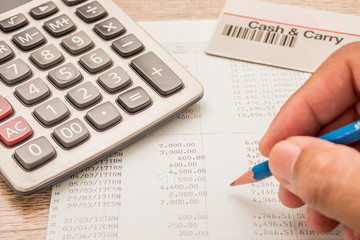 The fingers are holding the pencil. Below is a calculator, a bank book, a cash card placed on a wooden desk.