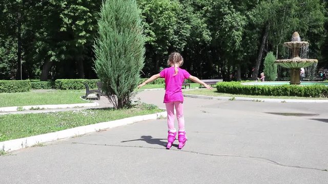 A little girl skates on roller skates. The child rolls on the rollers in the park. Rollerblading In The Park. Girl learns to ride a roller skate.