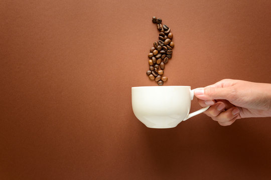 Hand holding cup of coffee with smoke from coffee beans brown paper background. Top view. Flat lay. copy space. Good morning concept.
