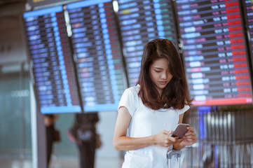 woman in international airport using her mobile phone near the flight information board,