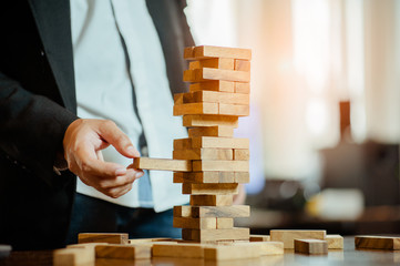 business man hand  pulling out or placing wood block on the tower in modern office. plan and strategy in business. blur for background.