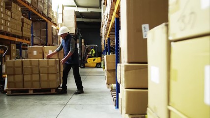 Senior male warehouse worker unloading boxes from a pallet truck. - Powered by Adobe