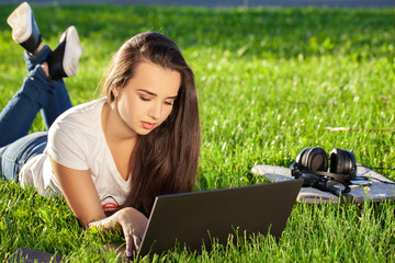 Young woman using laptop in the park lying on the green grass. Leisure time activity concept.