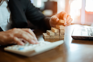plan and strategy in business.risk concept.hand of man has piling up and stacking a wooden block.Businessman Building The Success.using calculator to calculate.
