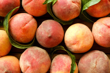 Bunch of ripe freshly picked organic peaches in pile on wooden tray of farmers market. Peach harvest heap. Healthy vegan raw snack. Clean eating concept. Cropped shot, background, top view, flat lay.
