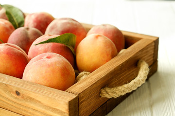 Bunch of ripe organic peaches in pile on wooden tray tray with rope handles on white wood textured table. Local produce harvest heap. Clean eating concept. Background, top view, close up, copy space.