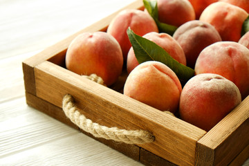Bunch of ripe organic peaches in pile on wooden tray tray with rope handles on white wood textured table. Local produce harvest heap. Clean eating concept. Background, top view, close up, copy space.