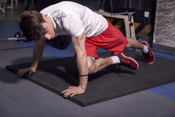 Fototapeta na wymiar one young man, exercise in gym indoors, one leg complicated plank sideways.