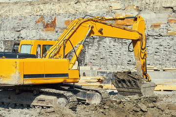 A large yellow excavator digs a foundation pit for the construction of a large residential complex. The bucket heats the ground. Building massive machinery. The initial stage of the new construction 