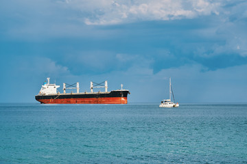 View of the sea. A large cargo ship stands in the roadstead, and a yacht anchored nearby. Panorama of the sea and sky. Sea idyll. Beautiful clouds before sunset of the day
