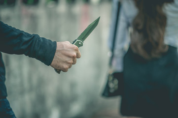 A bandit holds a knife. In order to attack and steal a woman's belongings from the back.