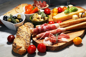 Italian antipasti wine snacks set. Cheese variety, Mediterranean olives, crudo, Prosciutto di Parma, salami and wine in glasses over stone grunge background.