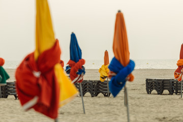 Beach umbrellas on foggy morning in Deauville, fashionable holiday resort in Normandy, France. Folded colorful parasols and lounge chairs on the empty beach. Leisure and seaside vacations concept.