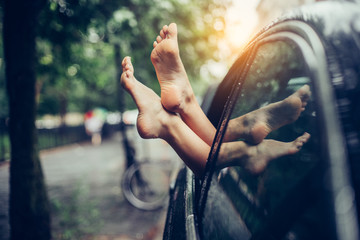 Female legs stick out of the car window. Woman having fun and relaxing in a car drung road trip.