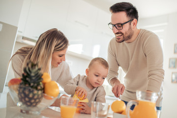 Obraz na płótnie Canvas Cheerful young family making orange juice