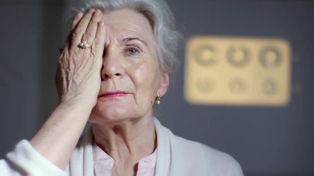 Tracking shot of senior woman covering one eye with hand and looking at eye chart while testing eyesight in clinic