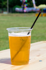 Cold beer in a plastic cup on wooden table at sunny day.