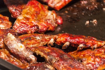Ribs detail on the barbecue. Group of Grilled pork ribs on the grill. Unhealthy fatty food. Risk of obesity. Blurred background.