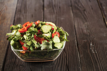 Vegetable salad with fresh tamata vegetables, cucumbers, lettuce, onions and arugula on a wooden table in a glass bowl. Vegetarian food salad. The concept of a healthy diet.