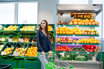Shopping woman looking at the shelves in the supermarket with shopping cart.  Portrait of a young girl in a market store at fruits and vegetables section.