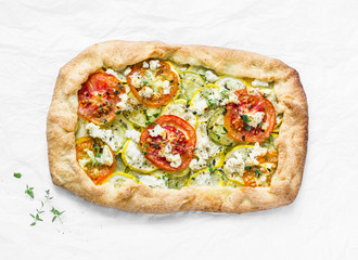 Feta, zucchini, tomatoes, thyme savory pie on a light background, top view. Delicious snack, appetizer in a mediterranean style