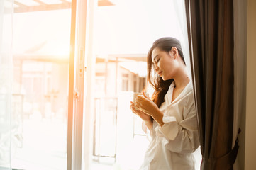 Woman holding a cup of coffee in her hands.Woman drinking coffee at home with sunrise at  window .