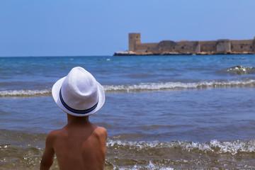 Fototapeta na wymiar summer and travel concept . boy with white hat is sitting by the sea