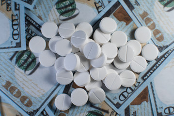 White pills on one hundred dollar bills close up. Medicine price concept.