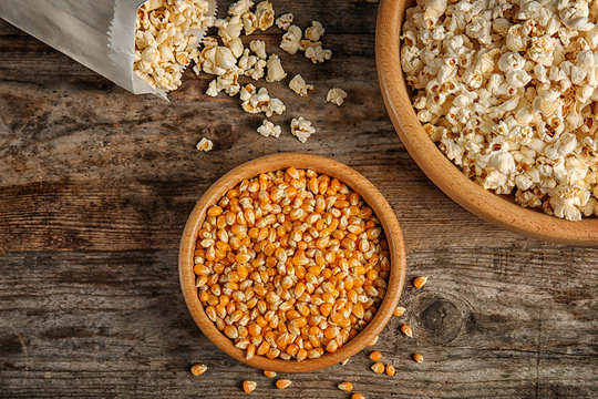 Delicious popcorn and kernels on wooden table, top view