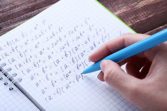 Female hand writing maths formulas in exercise book