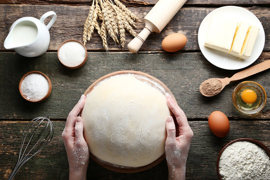 Female hands holding raw dough with eggs and butter on wooden table
