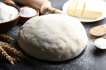 Raw dough with butter on plate and flour on black wooden table