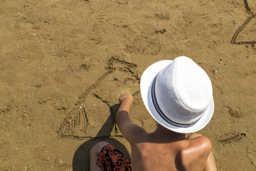 Fototapeta na wymiar summer and travel concept . boy with white hat plays and draws on the beach
