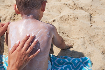 mother is putting on boy back a sunscreen on the beach.