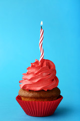 Tasty cupcake with candle on blue background