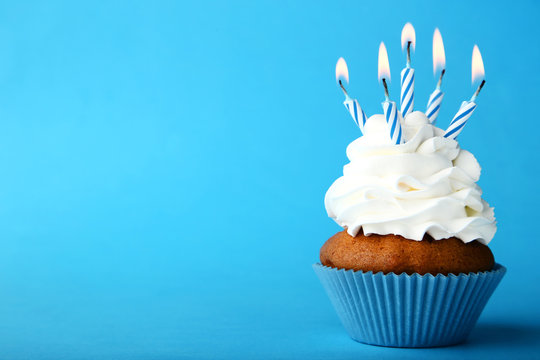 Tasty cupcake with candles on blue background