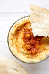 Hummus in bowl with spices and pita bread on a white wooden table, view from above. Closeup.