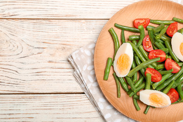 Plate with tasty green beans, eggs and  tomatoes on wooden table, top view