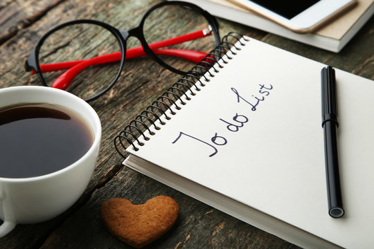 To do list in notepad with cup of coffee nd glasses on grey wooden table