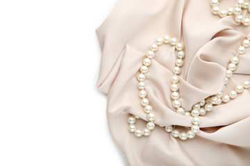 Pearl necklace with beige satin fabric on white background