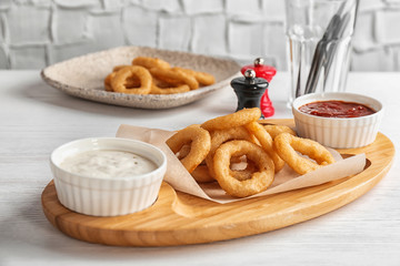 Wooden board with tasty onion rings and sauces on table