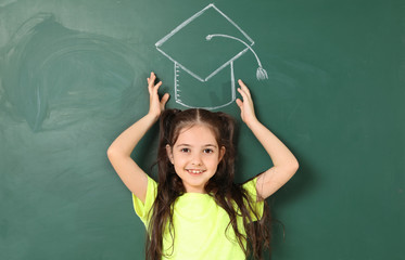 Fototapeta na wymiar Little school child near chalkboard with drawing of graduate cap