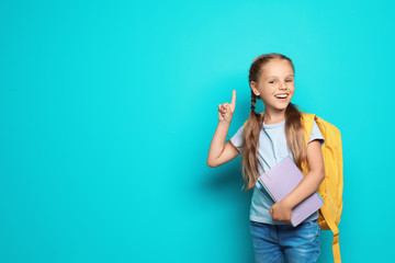 Little school child with backpack and copybook on color background