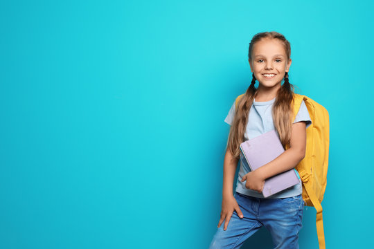 Little school child with backpack and copybook on color background