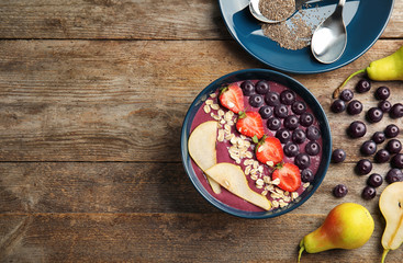 Flat lay composition with bowl of tasty acai smoothie on wooden table